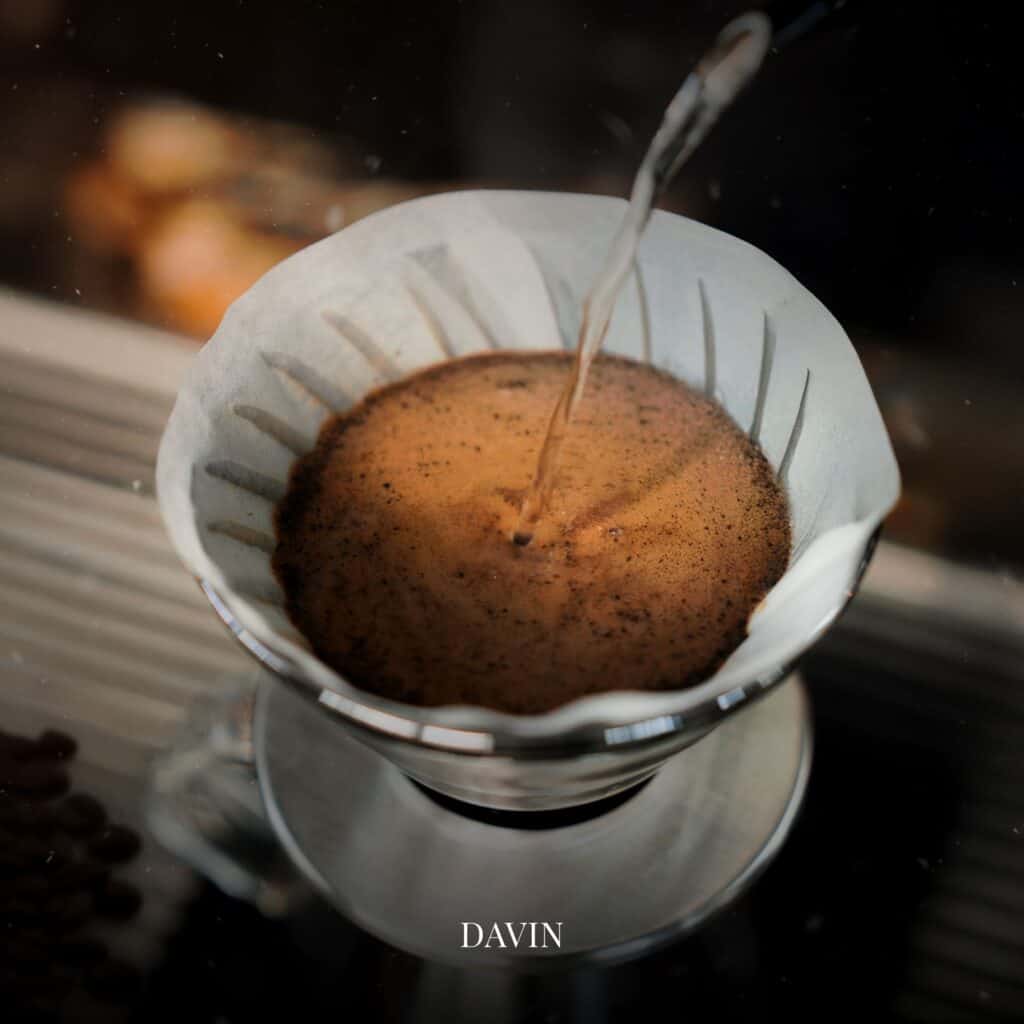 A close-up shot capturing the moment hot water is poured over coffee grounds in a V60 filter during pour-over brewing.