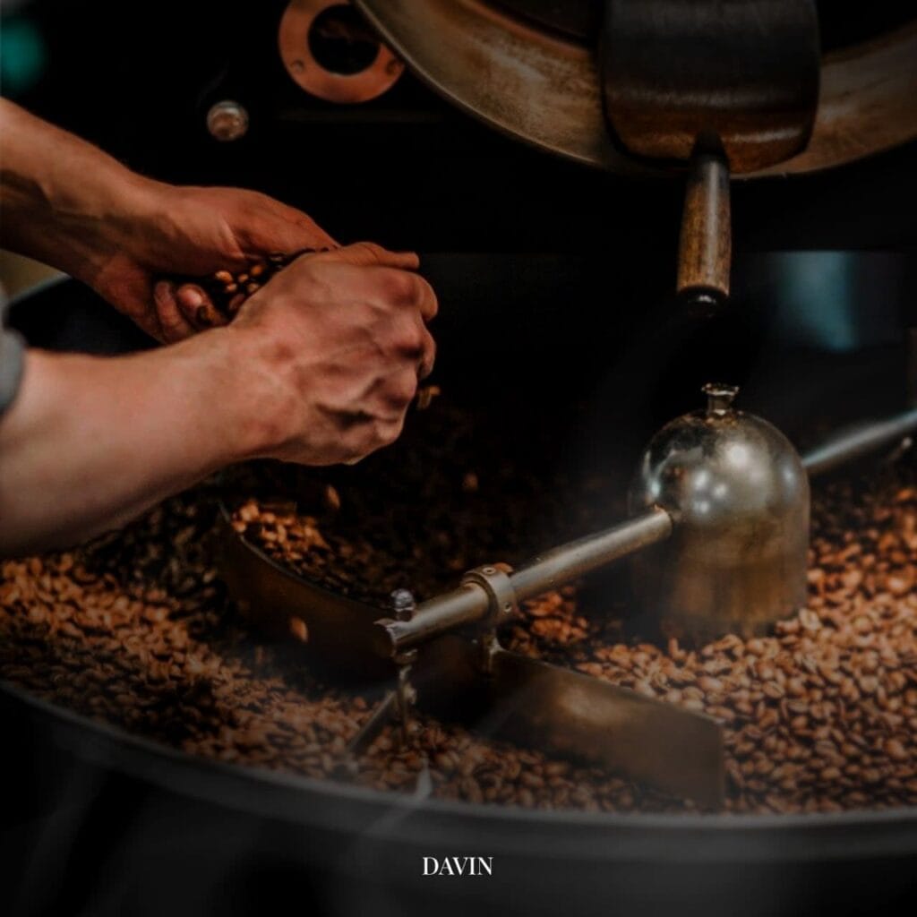 ภาพระยะใกล้ของมือผู้เชี่ยวชาญขณะกำลังตรวจสอบเมล็ดกาแฟในเครื่องคั่ว แสดงความพิถีพิถันในกระบวนการคั่วกาแฟสเปเชียลตี้ของ Davin Cafe.