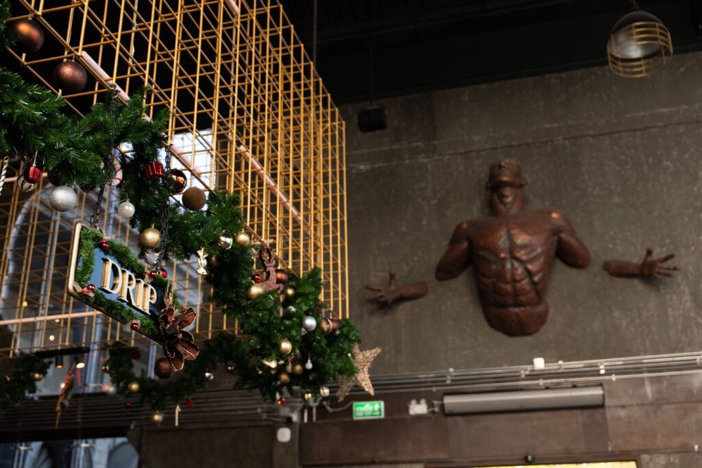 An industrial art–style event venue interior decorated for Christmas 2025, featuring golden metal structures, artistic sculptures, and festive Christmas garlands, perfect for unique Christmas parties, year-end celebrations, and premium holiday events