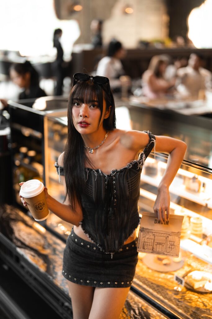 A customer posing with a drink beside a warmly lit bakery counter at Davin Cafe, capturing a soft and premium café atmosphere ideal for aesthetic-focused content