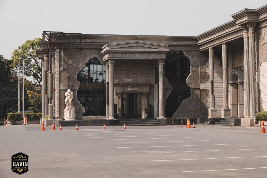 The exterior of Davin Cafe showcasing grand Roman-inspired architecture with large columns and spacious parking, offering a visually striking entrance for photo-focused visitors seeking both convenience and aesthetic appeal