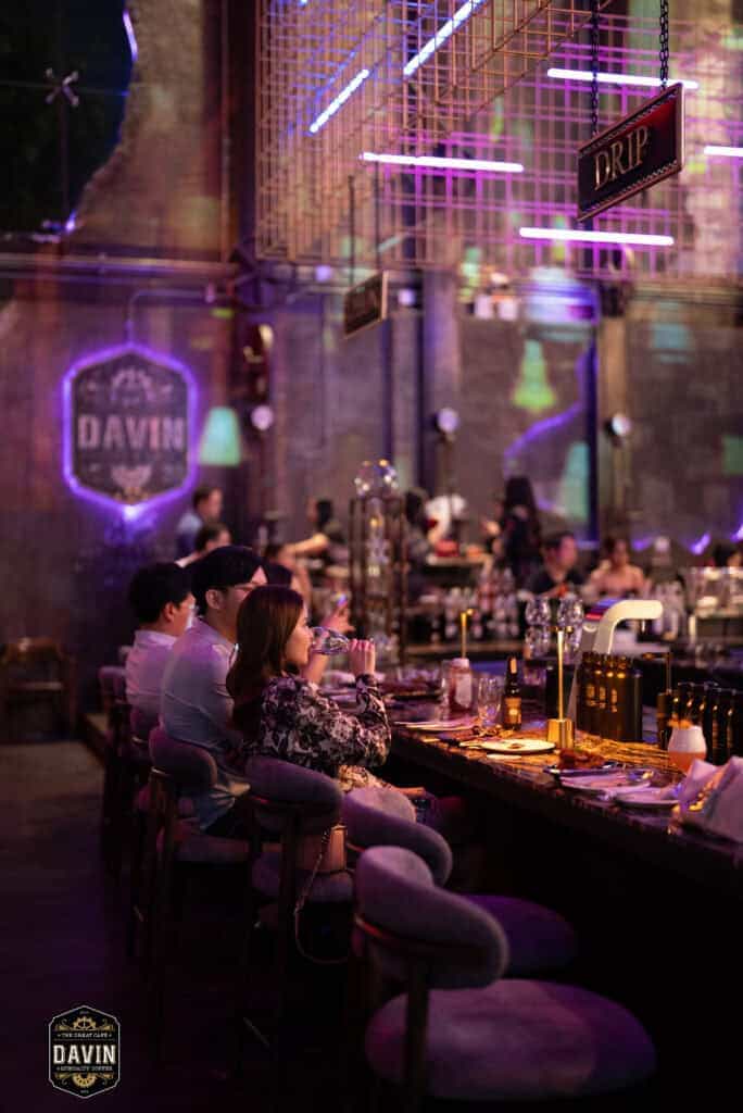 บรรยากาศผู้ร่วมงานนั่งบริเวณเคาน์เตอร์บาร์ของ Davin Cafe พร้อมแสงสีและพื้นที่ภายในร้านที่รองรับกิจกรรมได้หลากหลาย เหมาะสำหรับใช้เป็นสถานที่จัด Fan Meet ในกรุงเทพที่ต้องการทั้งมุมพบปะ พื้นที่นั่ง อาหาร เครื่องดื่ม และประสบการณ์งานอีเวนต์ที่ดูพรีเมียม