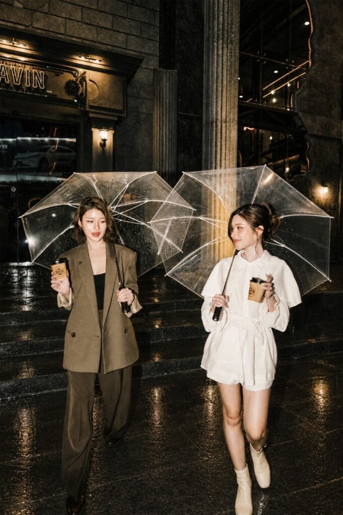 คาเฟ่หน้าฝน รามอินทรา DAVIN CAFE สองสาวถือร่มใสและกาแฟ ท่ามกลางบรรยากาศฝนตกหน้าร้านสไตล์ยุโรป